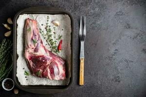 Raw fresh Lamb Meat shank, herbs and fork on black stone background photo