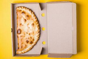 Closed pizza calzone in a packing box on a yellow background photo