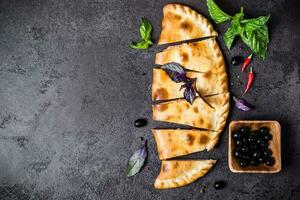 Closed pizza calzone is cut into pieces on black table photo