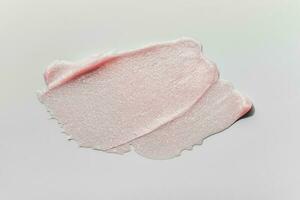 Smears of transparent pink lip gloss or moisturizer with glitter on grey background. Body highlighter swatch photo