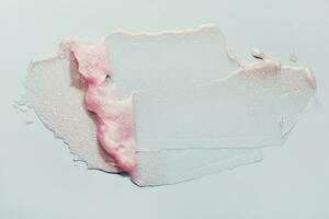 Smears of transparent pink lip gloss or moisturizer with glitter on grey background. Body highlighter swatch photo