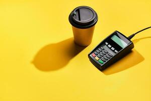 POS payment terminal and coffee on yellow background. Minimal financial service concept. Trendy shadows, copy space photo