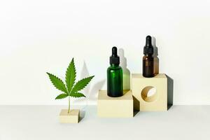 Cosmetic products with CBD oil and hemp extract. Glass bottles and hemp leaf on abstract geometric podiums with trendy shadows photo