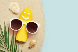 Yellow tube with happy sunscreen face and sunglasses. Sun Ultraviolet protection cosmetics product creative concept photo