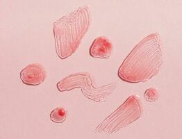 Smears of transparent shining lip gloss on a pink background photo