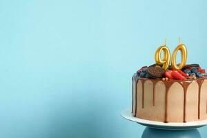 chocolate cumpleaños pastel con bayas, galletas y número noventa dorado velas en azul pared fondo, Copiar espacio foto