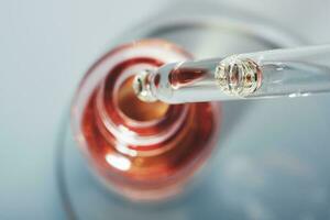 Oil or Serum bottle and pipette in petri dish on grey background. Pink cosmetic product, selective focus photo