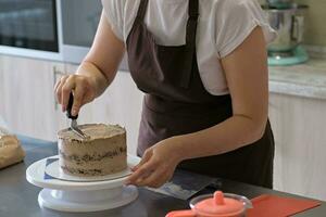 Woman pastry chef lines chocolate cream on chocolate cake, close-up. Cake making process, Selective focus photo