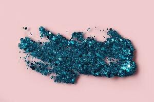 Blue glitter cosmetic product smear on pink background. Eye shadow, lip gloss and face glitter for holiday makeup swatch photo
