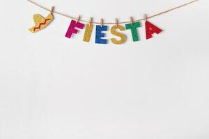 Fiesta word on pins against white wall background. Fragment of festive DIY decoration of interior. Cinco de mayo celebration photo