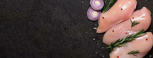 Raw chicken breast with spices and herbs on black stone background. Preparation for cooking, banner format photo