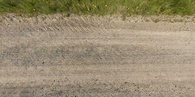 panorama of surface from above of gravel road with car tire tracks with roadside and grass photo