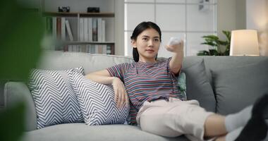 Young asian female watching television and holding a remote control photo