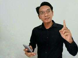 A portrait of a happy Asian man is smiling and holding her smartphone wearing a black shirt isolated by a white background photo