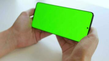 Female hands using a smartphone with a green screen in horizontal mode close-up. Chroma key. POV video