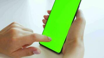 Female hands using a smartphone with a green screen in vertical mode close-up. Chroma key. POV video