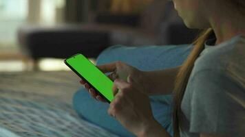 Woman at home lying on a couch and using smartphone with green mock-up screen in vertical mode. Girl browsing Internet, watching content, videos, blogs. POV. video