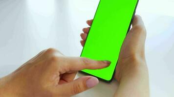 Female hands using a smartphone with a green screen in vertical mode close-up. Chroma key. POV video