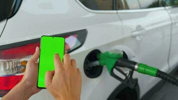 Woman using a mobile application in a smartphone to pay for refueling a car. Smartphone with a green screen. Chroma key video