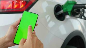 Woman using a mobile application in a smartphone to pay for refueling a car. Smartphone with a green screen. Chroma key video