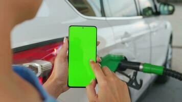 Woman using a mobile application in a smartphone to pay for refueling a car. Smartphone with a green screen. Chroma key video