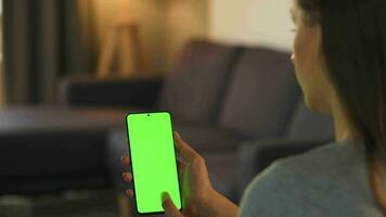 Woman at home lying on a couch and using smartphone with green mock-up screen in vertical mode. Girl browsing Internet, watching content, videos, blogs. POV. video