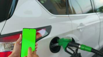 Woman using a mobile application in a smartphone to pay for refueling a car. Smartphone with a green screen. Chroma key video