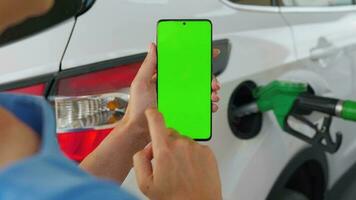 Woman using a mobile application in a smartphone to pay for refueling a car. Smartphone with a green screen. Chroma key video