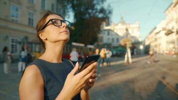 Woman walking down an old street and using smartphone at sunset. Communication, social networks, travel concept video