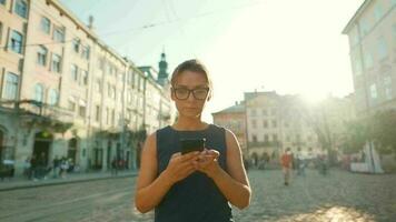 donna a piedi giù un vecchio strada e utilizzando smartphone a tramonto. comunicazione, sociale reti, viaggio concetto video