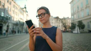 kvinna gående ner ett gammal gata och använder sig av smartphone på solnedgång. kommunikation, social nätverk, resa begrepp video