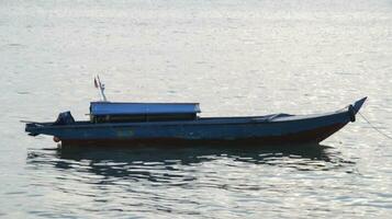 Small long wooden motor boat for fishing and transporting tied up or anchored at the shallow sea. photo