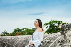 hermosa mujer en blanco vestir sentado solo a el paredes rodeando el colonial ciudad de cartagena Delaware indios foto