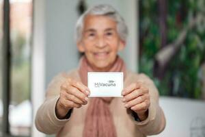 Senior woman at her home holding her vaccination certificate after getting the Covid-19 vaccine at a vaccination in Colombia. Authentic vaccination certificate. Real patient photo