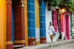 Beautiful woman on white dress walking alone at the colorful streets of the colonial walled city of Cartagena de Indias photo