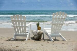 vacío blanco de madera sillas a un paradisíaco playa en el zona tropical en un hermosa soleado día foto