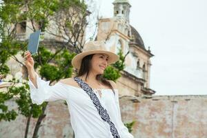 Beautiful young woman trying on hats to buy one from an street vendor in Cartagena de Indias walled city photo