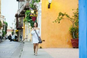 Beautiful woman on white dress walking alone at the colorful streets of the colonial walled city of Cartagena de Indias photo