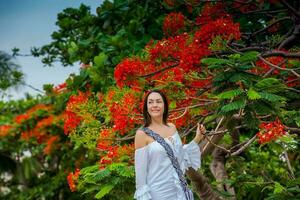 mujer en blanco vestir siguiente a un hermosa de flores árbol a el paredes rodeando el colonial ciudad de cartagena Delaware indios foto