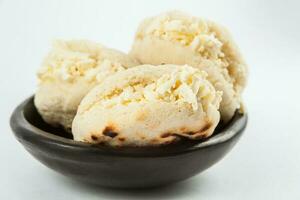 Colombian traditional white corn arepa stuffed with grated cheese in a black ceramic dish on white background photo