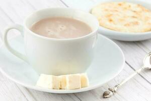 Cup of hot chocolate with cheese and arepa served in white dishware photo