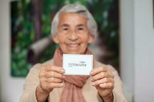 Senior woman at her home holding her vaccination certificate after getting the Covid-19 vaccine at a vaccination in Colombia. Authentic vaccination certificate. Real patient photo