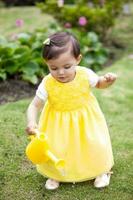 Sweet one year old baby girl dressed in yellow watering the plants at the garden photo