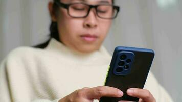 Happy young woman using mobile phone while sitting on sofa at home. Attractive woman holding smartphone checking social media, playing games, online shopping relaxing on sofa. video