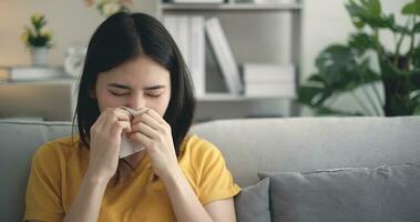 asiático joven mujer fiebre estornudar en soplo su nariz en papel pañuelo de papel a hogar foto