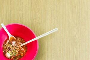 Asian noodle soup in a red bowl with wooden background,Spicy noodle,tom-yum-noodles, Top view,Copy space photo