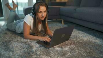 Frau ist Lügen auf das Boden, Arbeiten auf ein Laptop und hört zu zu Musik- auf Kopfhörer. Konzept von Fernbedienung arbeiten. video
