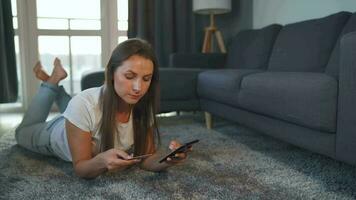 mujer es acostado en el piso y y hace un en línea compra utilizando un crédito tarjeta y teléfono inteligente en línea compras video