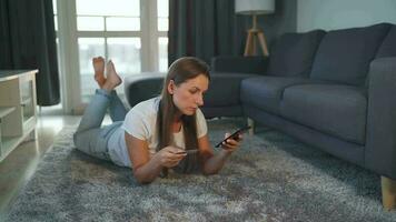 Woman is lying on the floor and and makes an online purchase using a credit card and smartphone. Online shopping video