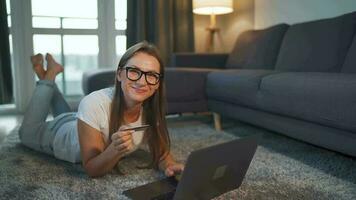 vrouw is aan het liegen Aan de verdieping en en maakt een online aankoop gebruik makend van een credit kaart en laptop. online winkelen, levensstijl video